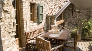 Un bâtiment rustique en pierre, doté d’une terrasse en bois, d’une table avec des chaises et d’un banc.