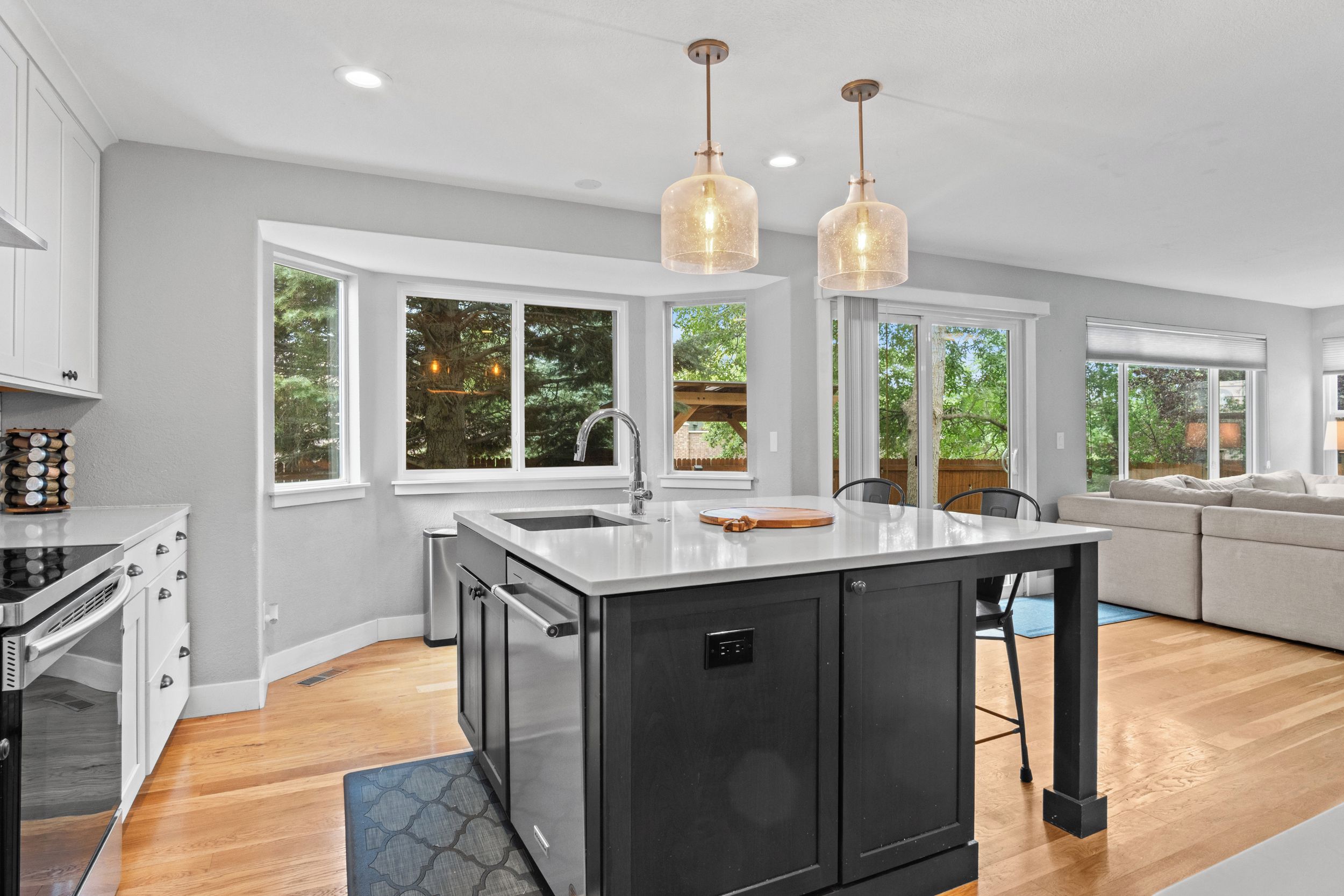 A modern kitchen with a central island, large windows, and pendant lighting.