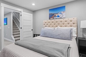 Une chambre à coucher avec un lit, une tête de lit, un tableau, un escalier et une porte.