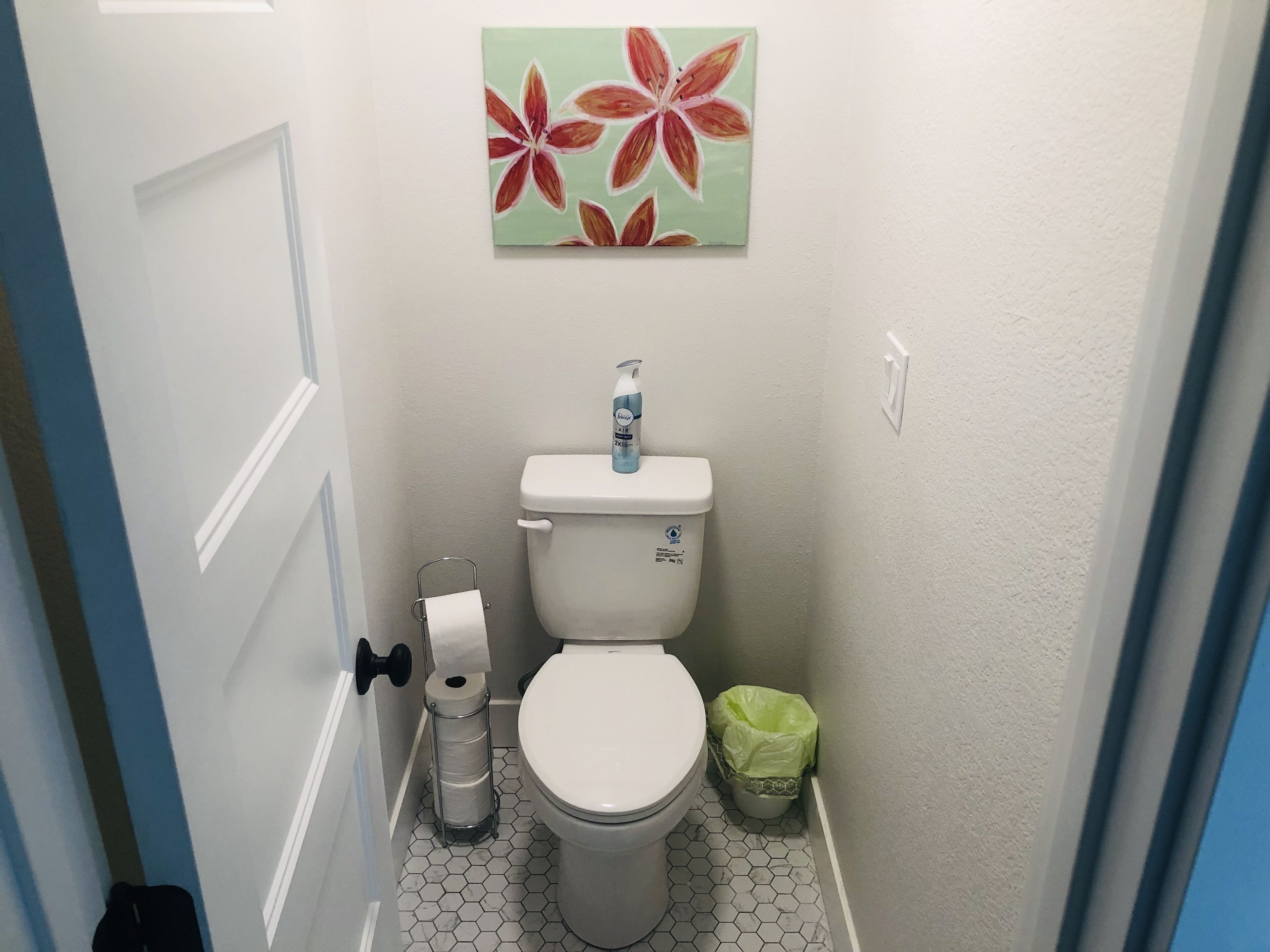 Un baño pequeño con inodoro, dispensador de papel higiénico y un cubo de basura.