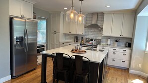 Uma cozinha moderna com eletrodomésticos de aço inoxidável, uma ilha central com cadeiras e iluminação pendente.