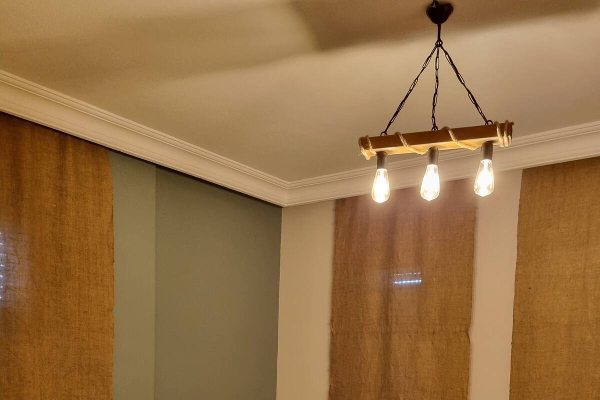 A bedroom with a bed, a bedside table, and a hanging light fixture.
