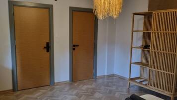 A hotel room with a bed, two doors, a woven light fixture, and a wooden shelf.
