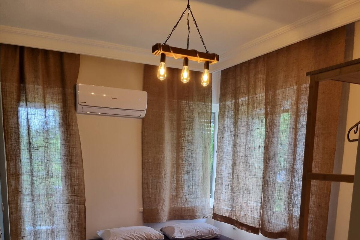 A room with a bed, a wooden floor, an air conditioning unit, and a hanging light fixture.