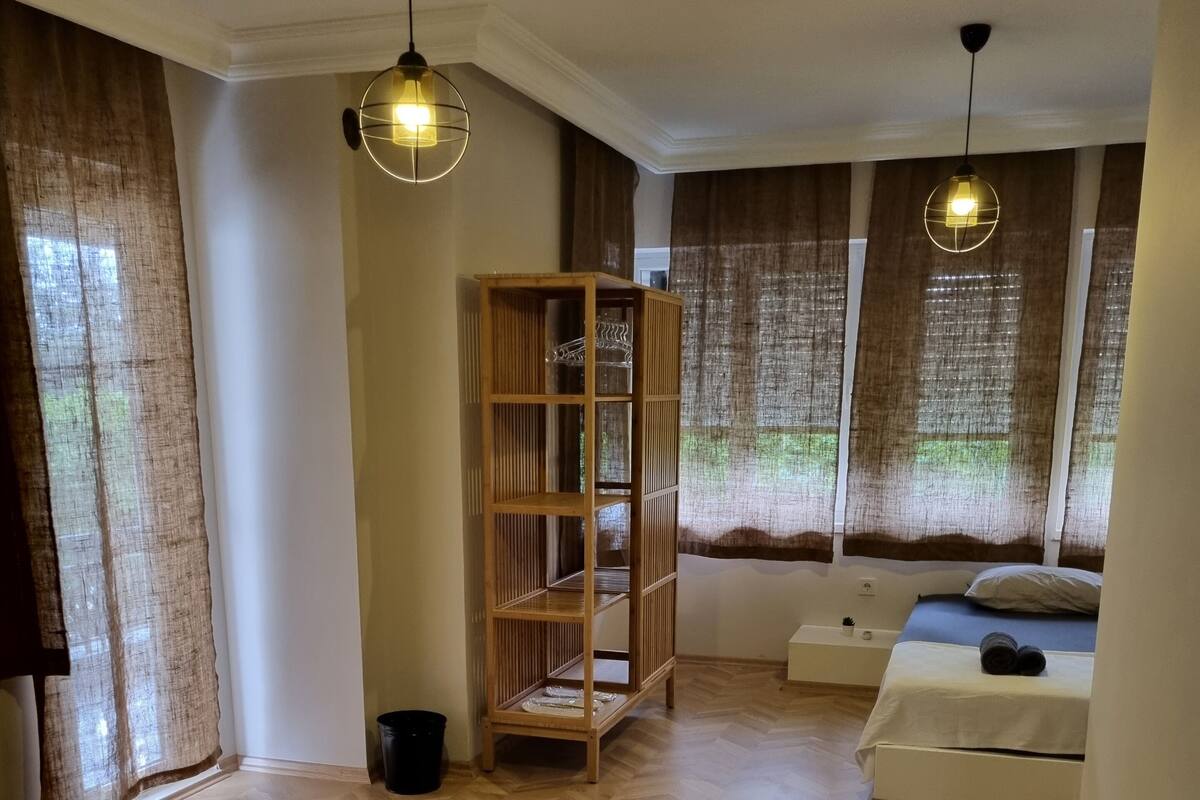A room with a herringbone wooden floor, a wooden shelving unit, a bed with a white mattress, and two pendant lights.