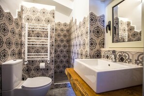 A bathroom with patterned tiles, a white toilet, a wooden vanity with a sink, and a mirror. - B&B La Mia Valigia (San Lucido)