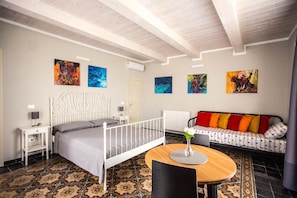 A bedroom with a bed, a round wooden table, a sofa, and artwork on the walls. - B&B La Mia Valigia (San Lucido)