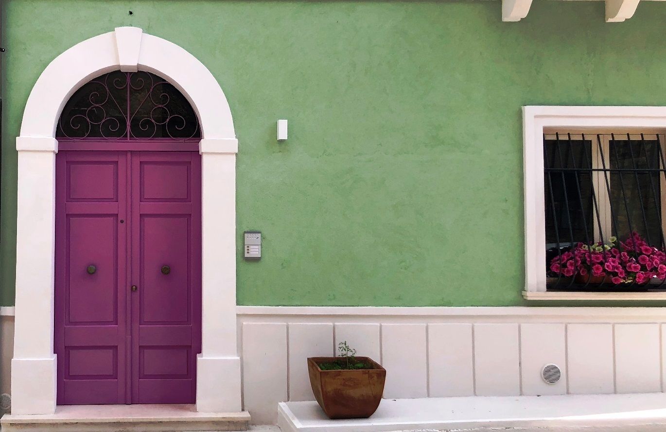 A green building with a purple door and a window with pink flowers.