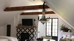 A cozy loft-style living space with exposed wooden beams, a fireplace, a dining area, and a comfortable seating arrangement. - THE BARN ON PASCAL... A lovely circa 1900 refurbished barn. (Rockport)
