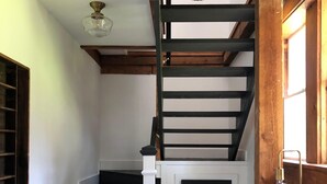A staircase with black steps and white risers, a wooden ceiling beam, and a white wall with a window. - THE BARN ON PASCAL... A lovely circa 1900 refurbished barn. (Rockport)