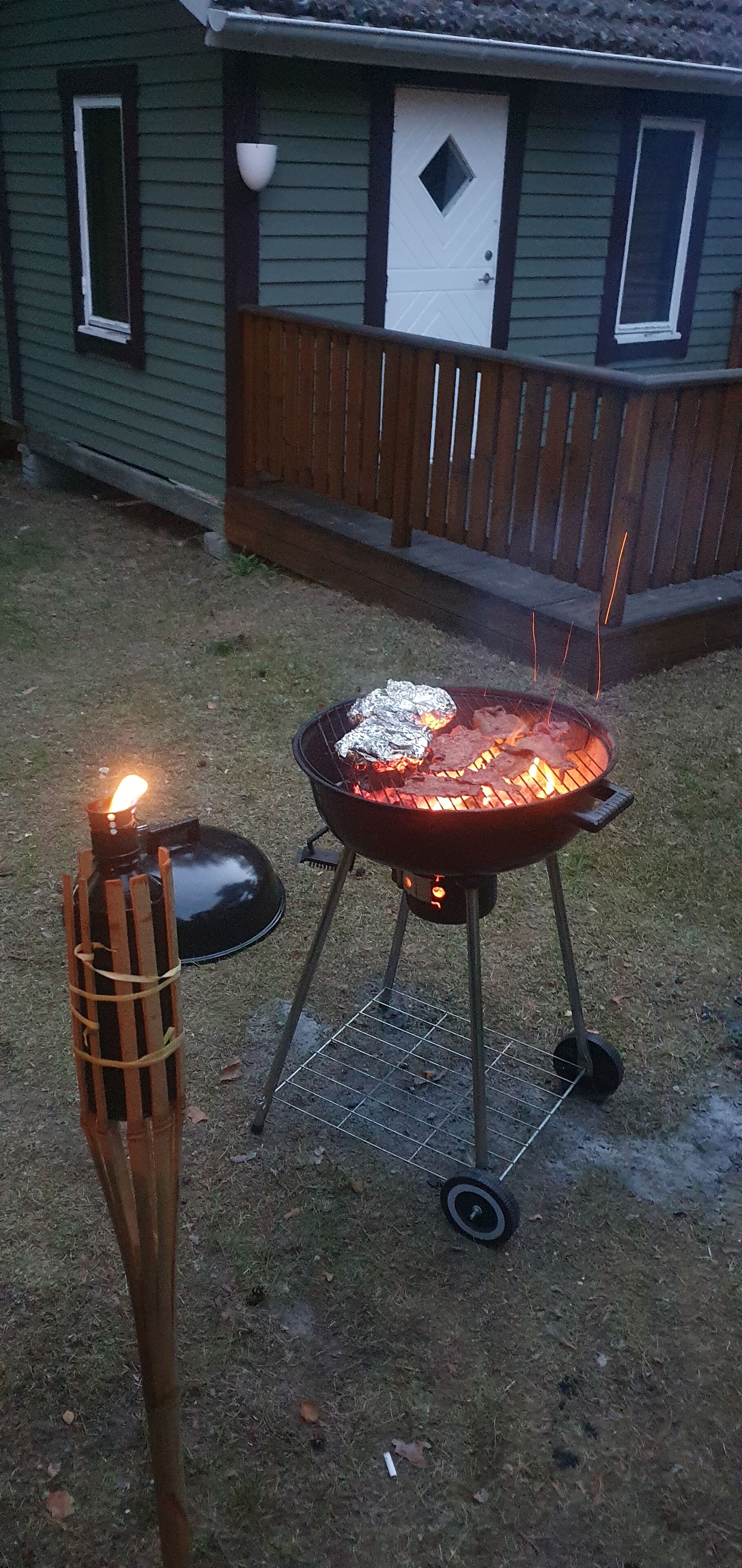Ein Hinterhof mit einem tragbaren Grill, einer beleuchteten Tiki-Fackel und einem Haus im Hintergrund.