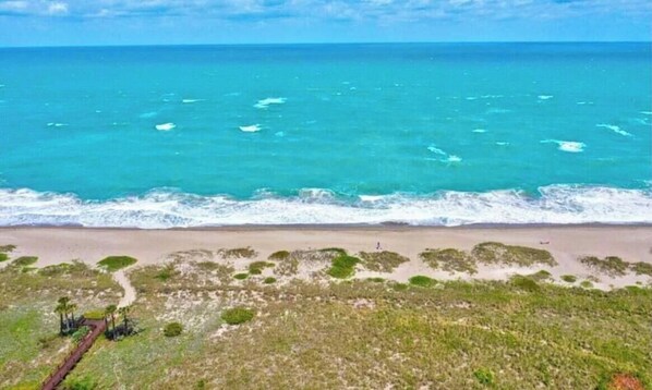 Ein Strand mit klarem türkisfarbenem Wasser, sandigem Ufer und spärlicher Vegetation.