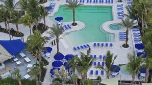 A resort pool area with multiple lounge chairs and umbrellas, surrounded by palm trees. - Luxurious Beach Resort Atmosphere Getaway (Fort pierce)