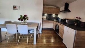 Eine moderne Küche mit Holzausstattung, einem Geschirrspüler von Bosch sowie einem Essbereich mit Holztisch und weißen Stühlen.
