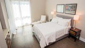 Un dormitorio ordenado con una cama grande, una silla, mesitas de noche y dos cuadros en la pared.