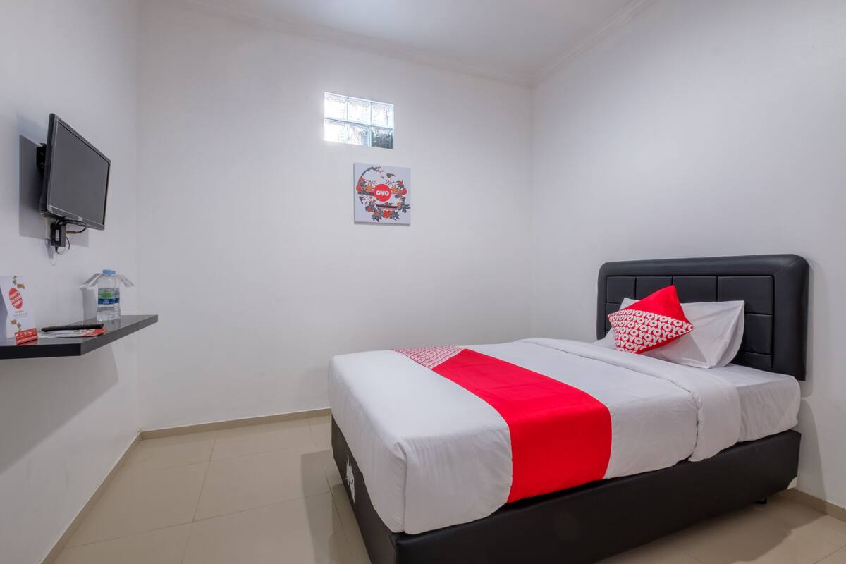 A bedroom with a bed, a TV mounted on the wall, a small window, and a shelf with items.