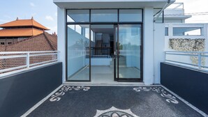 A modern building with large glass doors, a balcony with a patterned floor, and a traditional tiled roof in the background. - OYO 672 Bali Radiance Canggu (Tibubeneng)