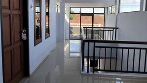 A clean, modern hallway with wooden doors, large windows, and a balcony with a metal railing. - OYO 672 Bali Radiance Canggu (Tibubeneng)