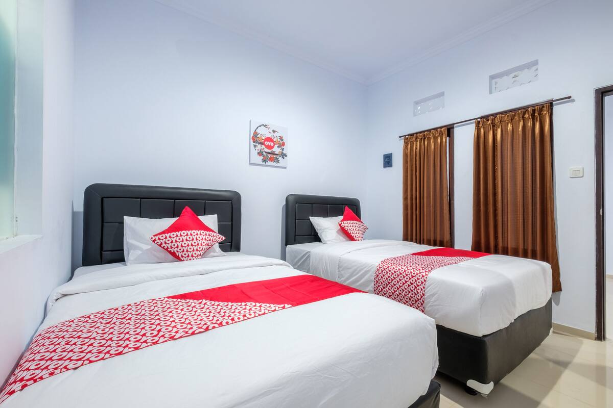 A hotel room with two beds, each with a black headboard, white bedding, and red accents.