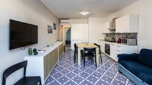 A compact kitchen with a dining area, a flat-screen TV mounted on the wall, and a blue patterned floor.
