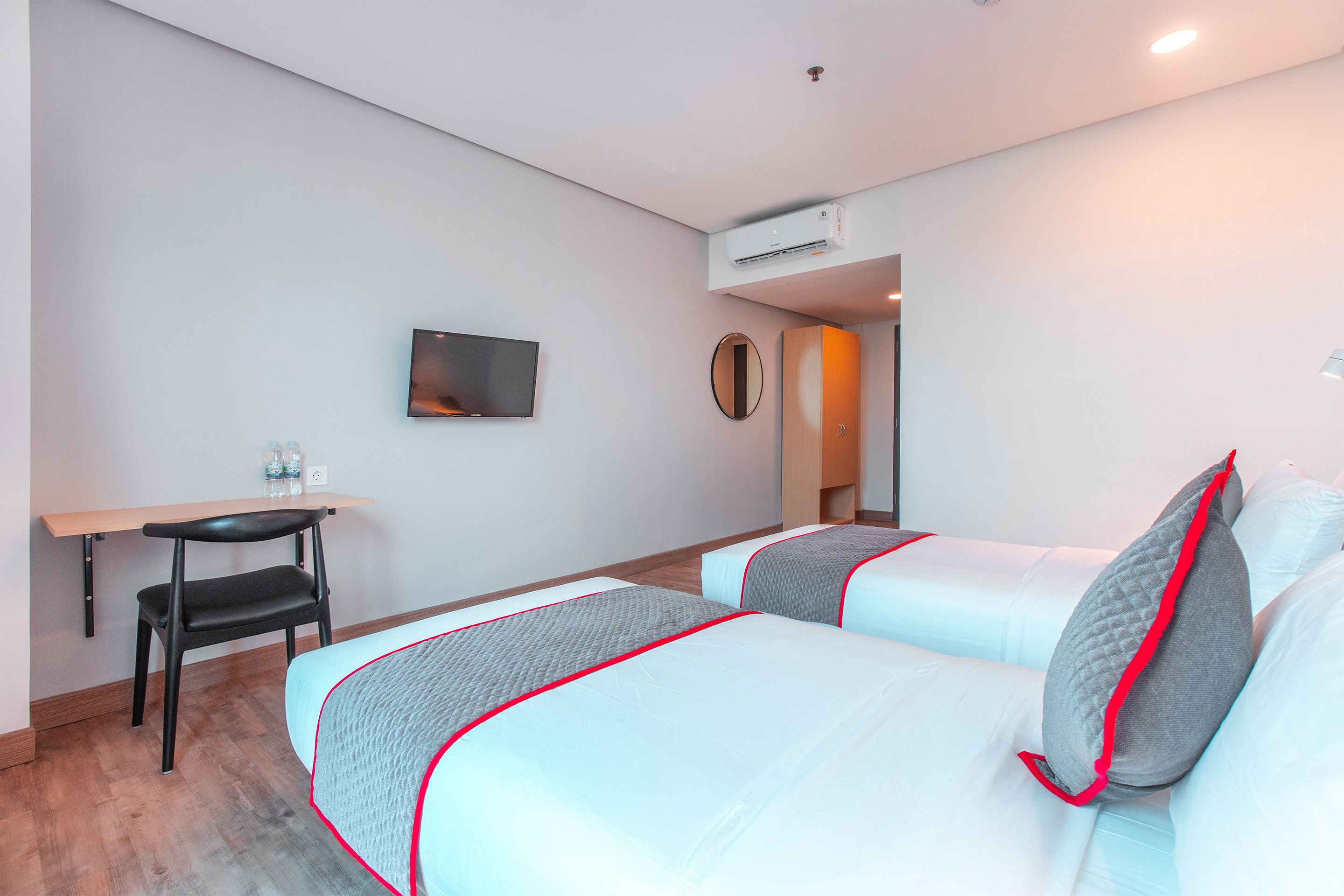 A hotel room with two beds, a desk, a chair, a TV, and an air conditioning unit.