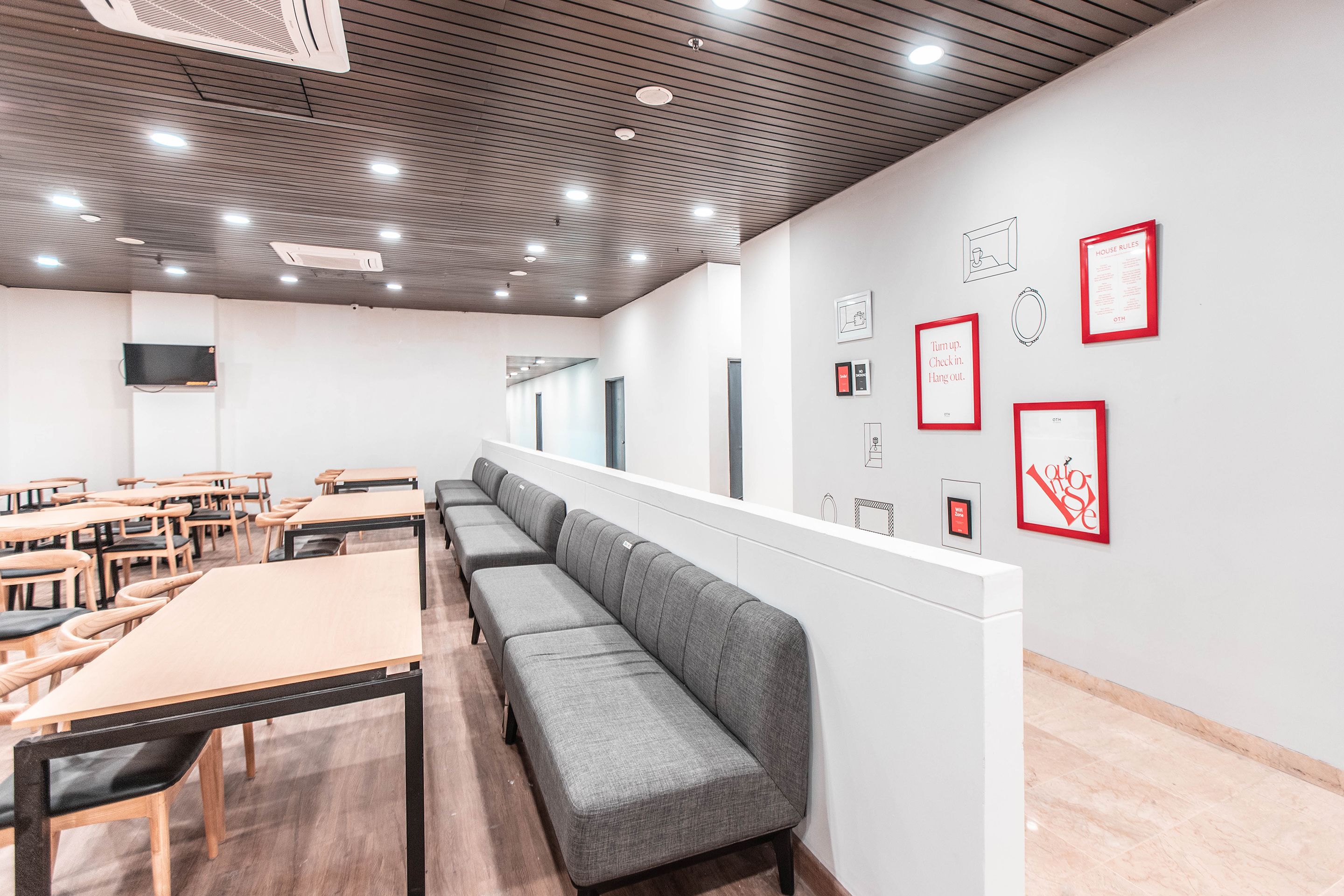 A modern conference room with long tables and benches, white walls, and framed artwork.