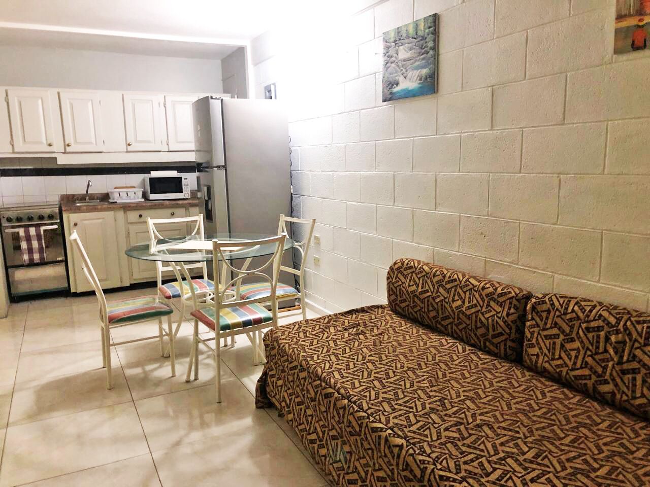 Un espacio habitable compacto con kitchenette, una mesa de comedor con sillas y un sofá estampado.
