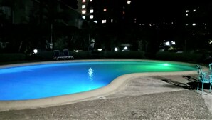 Ein Schwimmbad bei Nacht mit gewölbter Kante, umgeben von einer Betonplattform und einigen Liegestühlen.