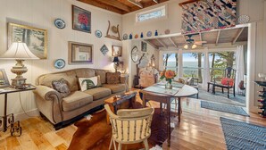 A cozy living room with a wooden ceiling, a dining table with a vase of flowers, and a view of the outdoors through large windows. - Amazing Mountain Views Special Rates Book Today (Mentone)