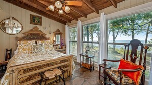 A bedroom with a large bed, a wooden ceiling fan, a window with a view of trees, and a chair with a red cushion. - Amazing Mountain Views Special Rates Book Today (Mentone)
