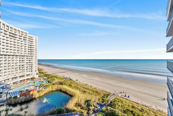 A hotel with a pool, beach view, and a small water body.
