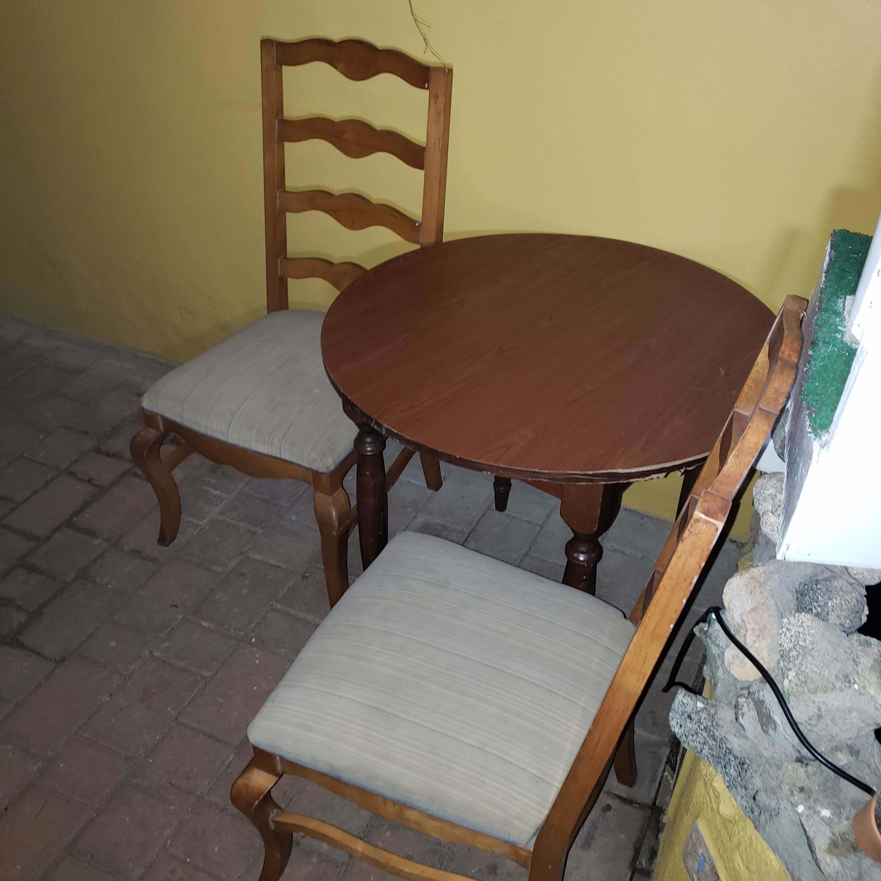 A round wooden dining table with two chairs, one with a cushioned seat and the other with a woven seat.