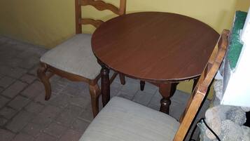 A round wooden dining table with two chairs, one with a cushioned seat and the other with a woven seat.