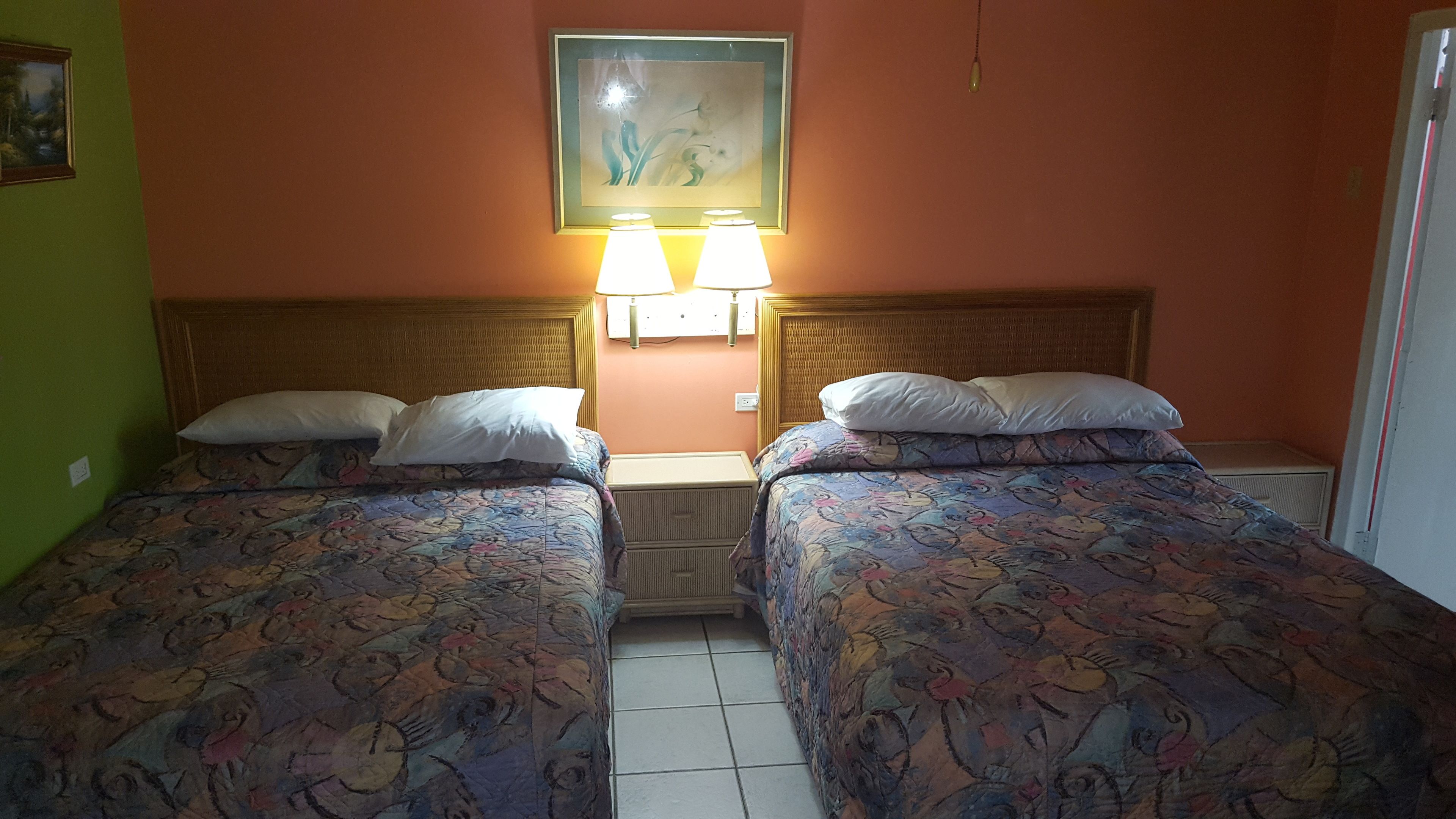 Una habitación con dos camas, cada una con ropa de cama estampada y almohadas blancas. Hay lámparas de pared sobre las camas y un cuadro en la pared.