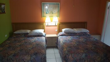 Una habitación con dos camas, cada una con ropa de cama estampada y almohadas blancas. Hay lámparas de pared sobre las camas y un cuadro en la pared.