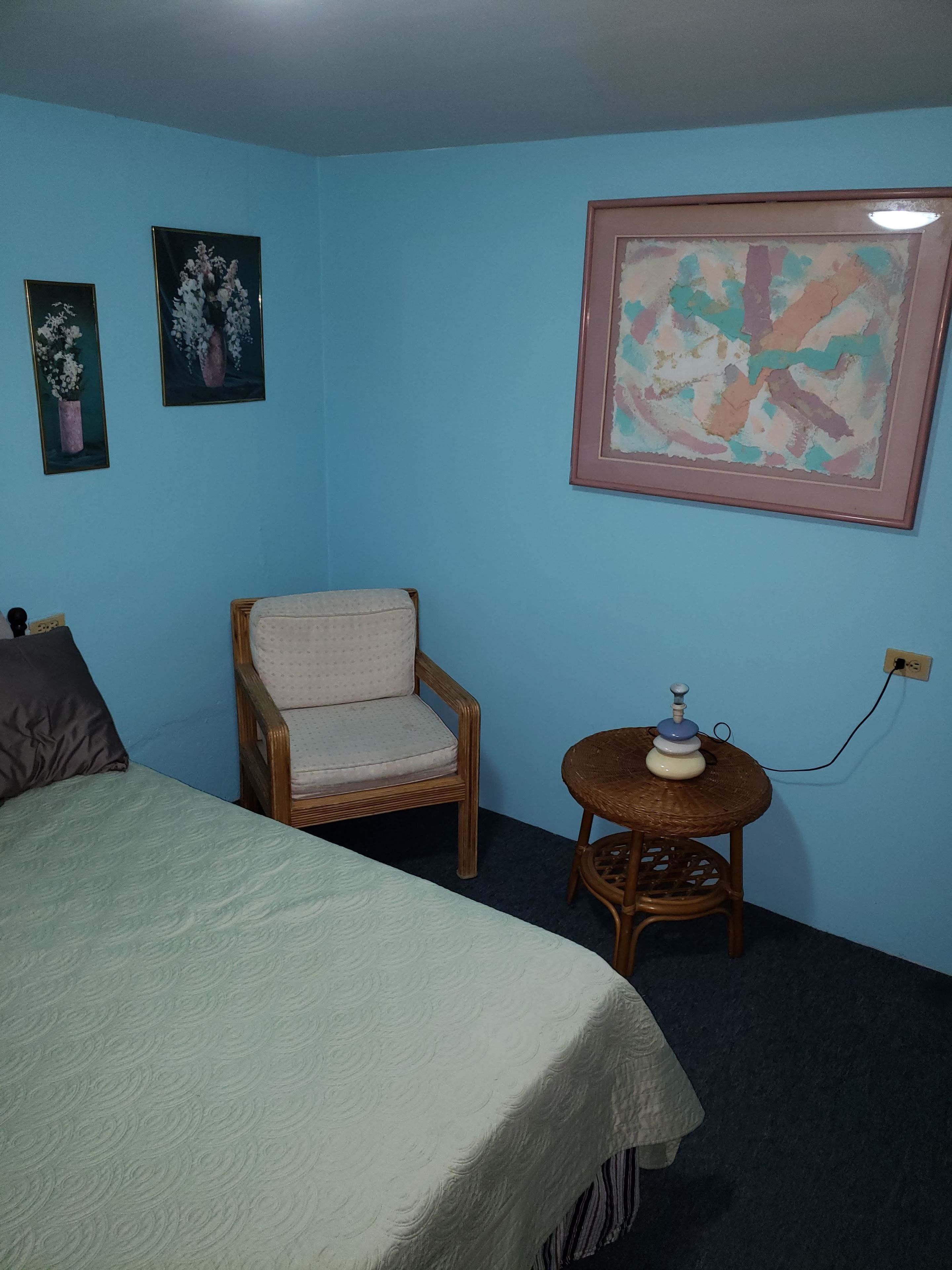 Una habitación con una cama, una silla, una pequeña mesa con una shisha y dos cuadros en la pared.