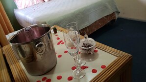 A hotel room with a bed, a bedside table with a pitcher, two glasses, and a small decorative item. - A1 Apartments Aruba (Oranjestad)