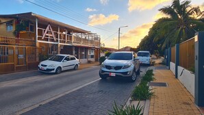 A street with two cars parked on the side, a building with a balcony, and a palm tree. - A1 Apartments Aruba (Oranjestad)