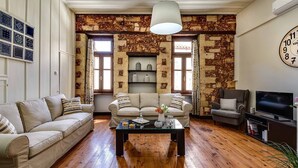 A living room with a stone wall, two sofas, a coffee table, and a television. - Casa Veneziana Chania, Casa Veneziana (Chania)