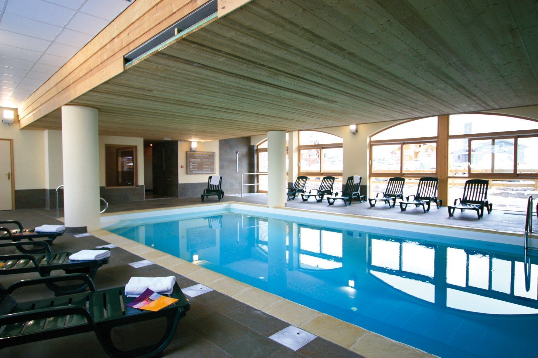 Une piscine intérieure dotée de chaises longues et d’un plafond en bois.