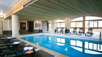 Une piscine intérieure dotée de chaises longues et d’un plafond en bois.
