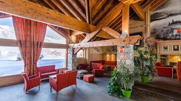 Un intérieur chaleureux avec des poutres en bois, des meubles rembourrés de tissu rouge et un mur en pierre.