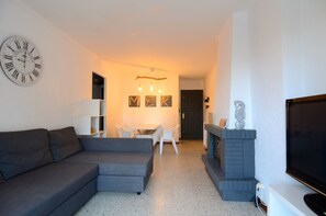 Una sala de estar con un sofá gris, televisor, chimenea y comedor con mesa y sillas.