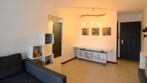 Un salon avec un canapé, des étagères blanches, un téléviseur fixé au mur et une porte.
