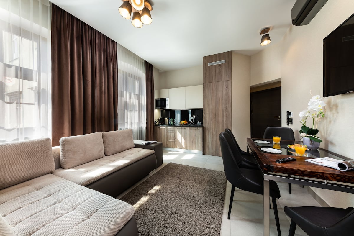 A modern living room with a sofa, dining table, chairs, and a kitchen area in the background.