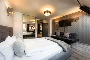 Habitación de hotel moderna con una cama grande, un televisor de pantalla plana en la pared y un espejo amplio sobre la cama.