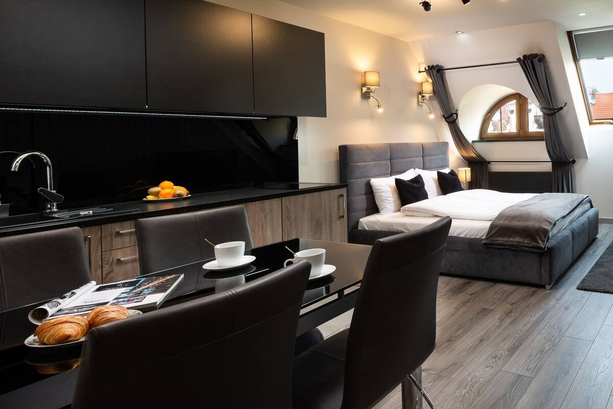 A modern hotel room with a kitchen, dining area, and a bed.