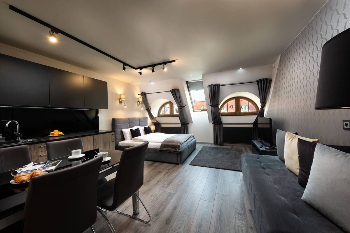 A modern, well-lit room with a bed, a sofa, a dining area, and a kitchen.