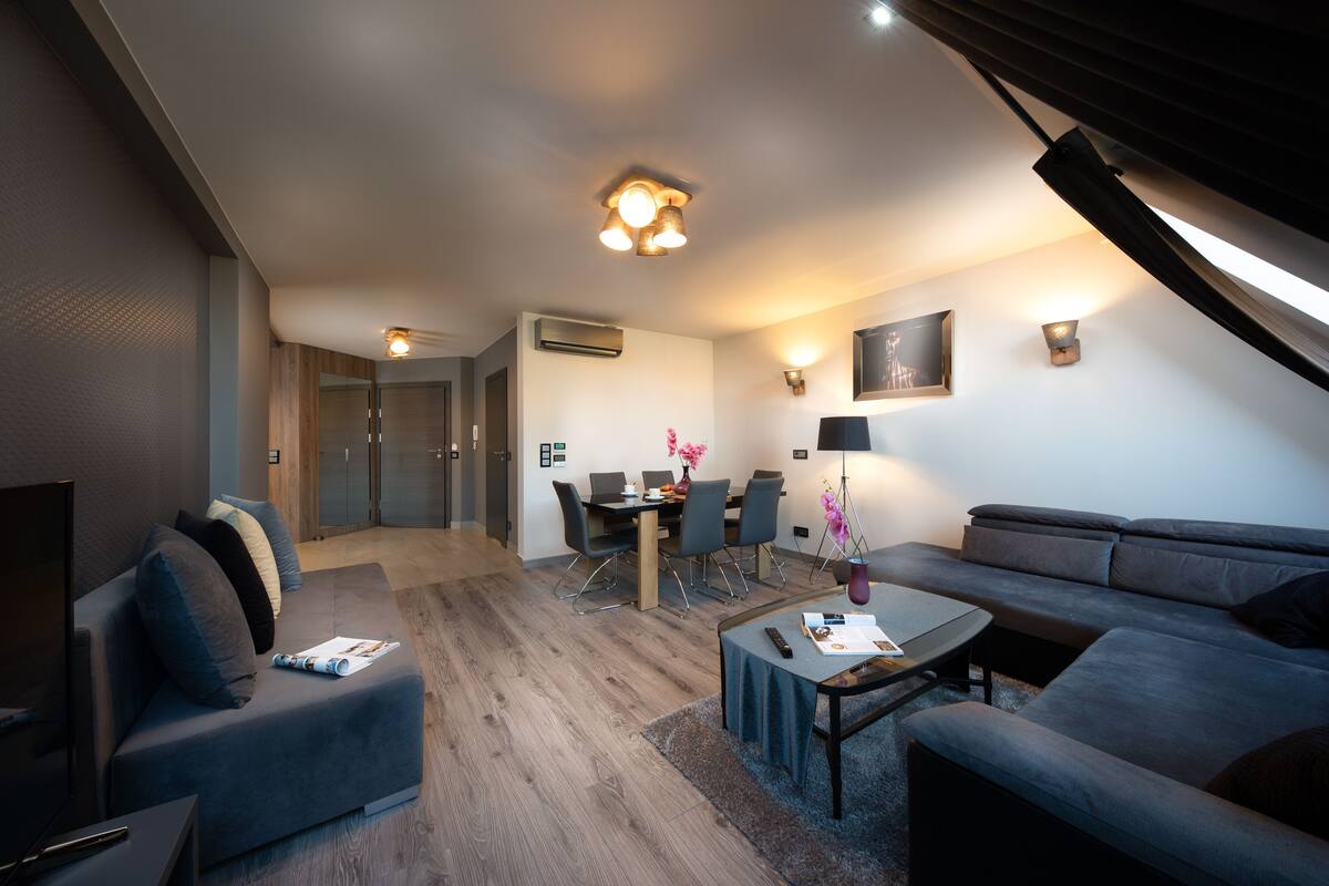 A modern living room with a sofa, coffee table, and a dining area with chairs and a table.