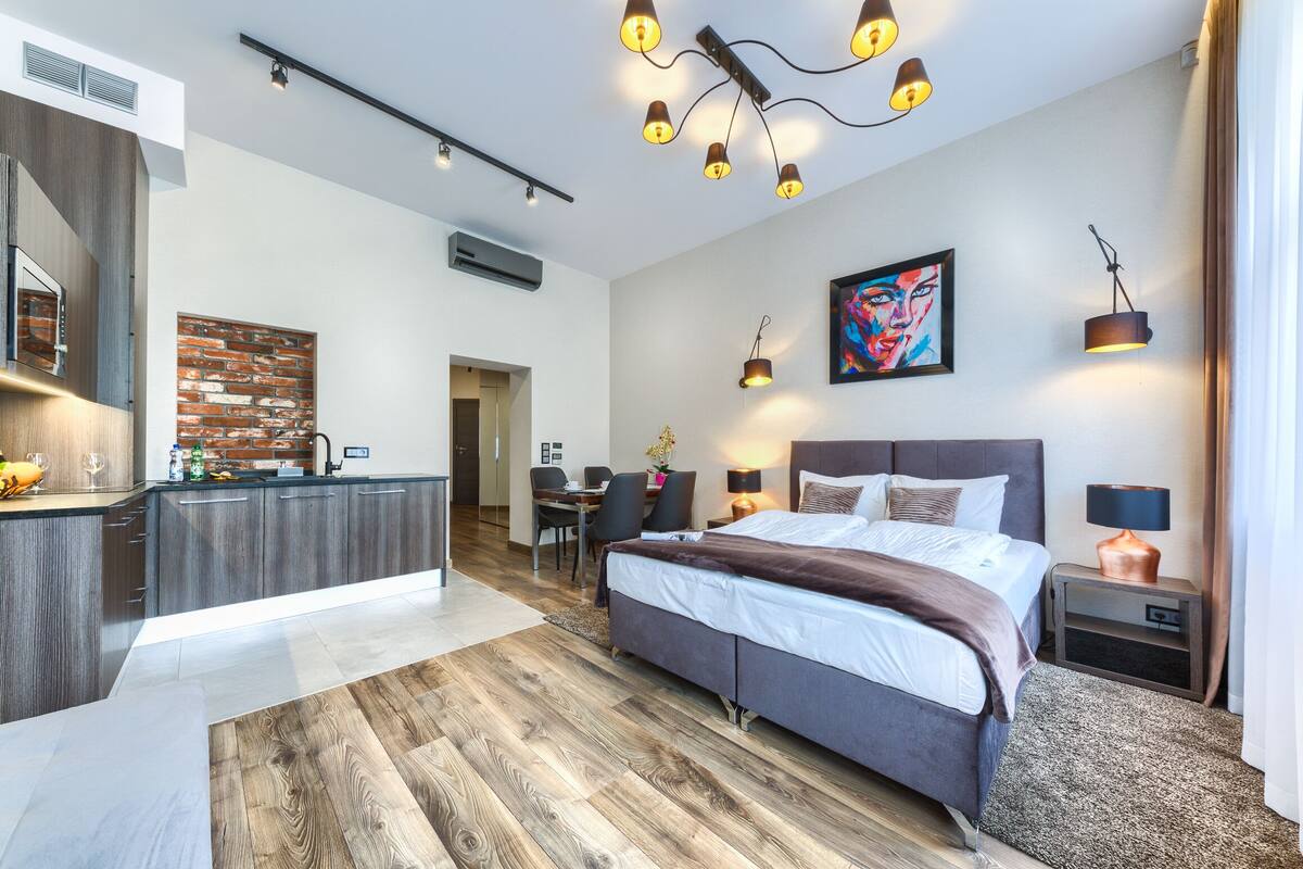 A modern hotel room with a large bed, a kitchen area, and a dining space.